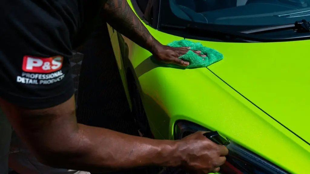 Detailer finishing green sports-car paint with a microfiber cloth